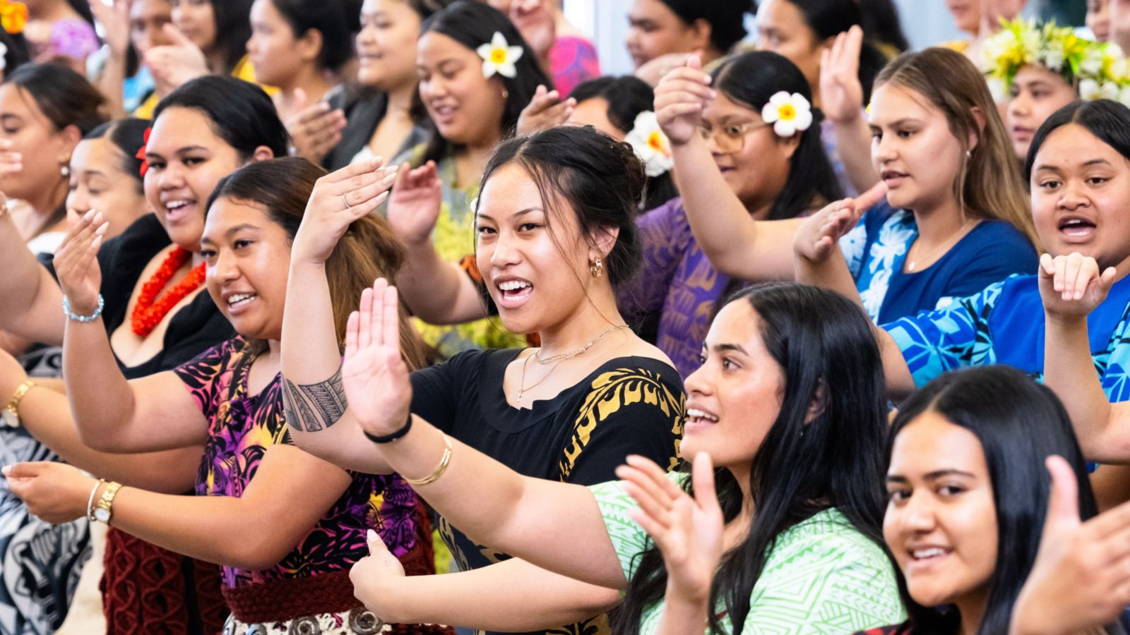 Cultural dance performance with participants in vibrant clothing and floral accessories.
