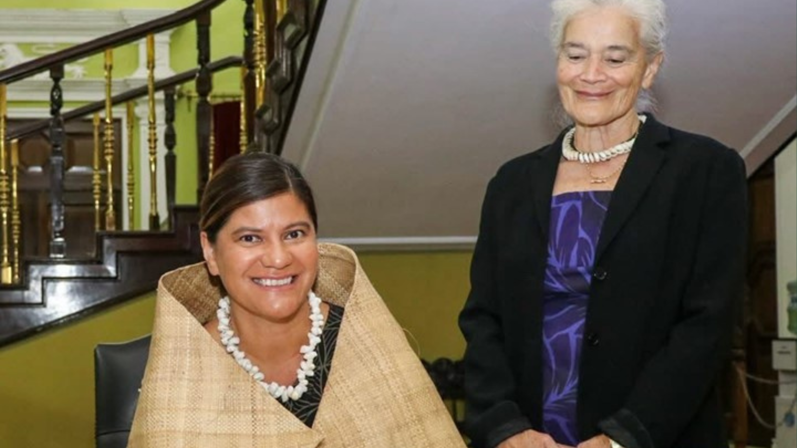 Emma Dunlop-Bennett is sitting at a desk smiling and Professor Peggy Fairbairn-Dunlop is standing behind her and smiling. 