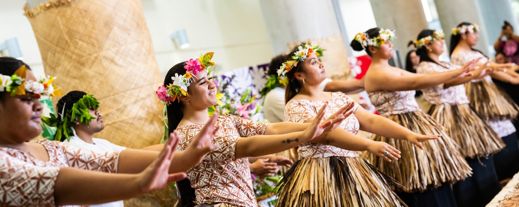Two rows of Pasifika dancers, inside, dressed in traditional clothing.