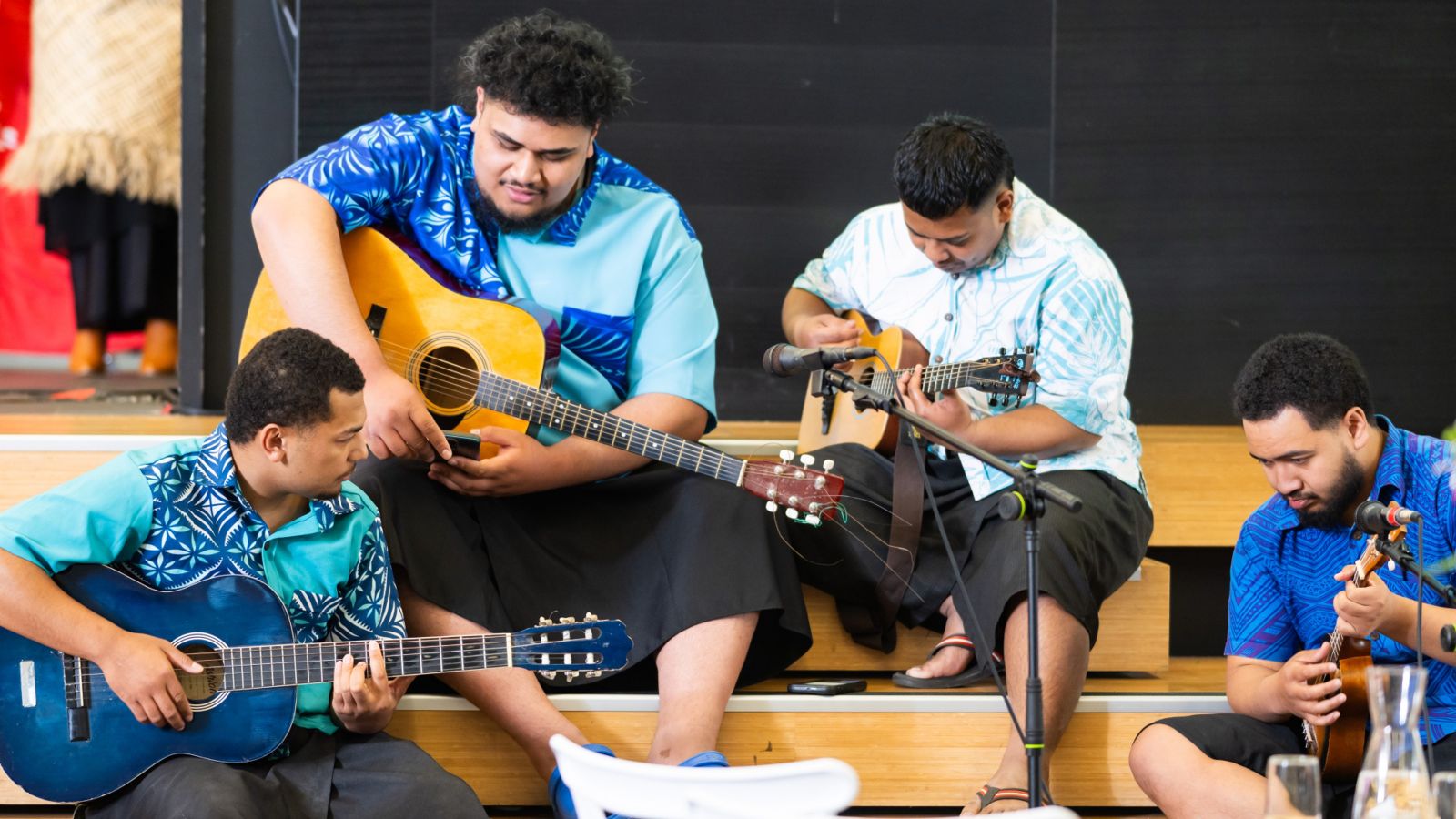 Four Pasifika boys sitting on the stage with guitars