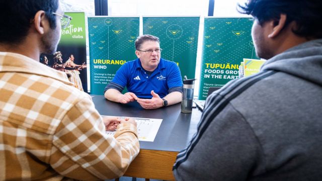 Man in blue Uni Rec shirt sitting behind a desk.