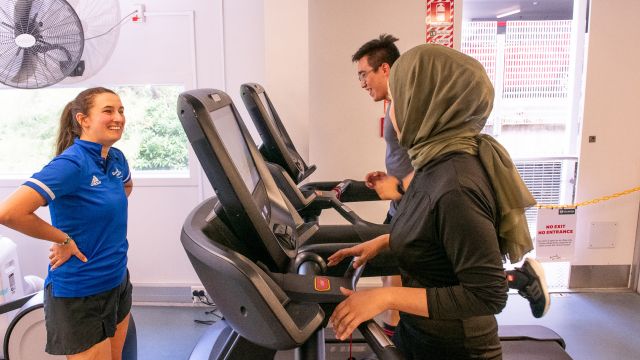 A gym staff member encourages two people running on treadmills.