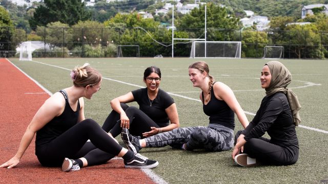 our students wearing exercise clothes laugh with each other while sitting on outdoor turf.