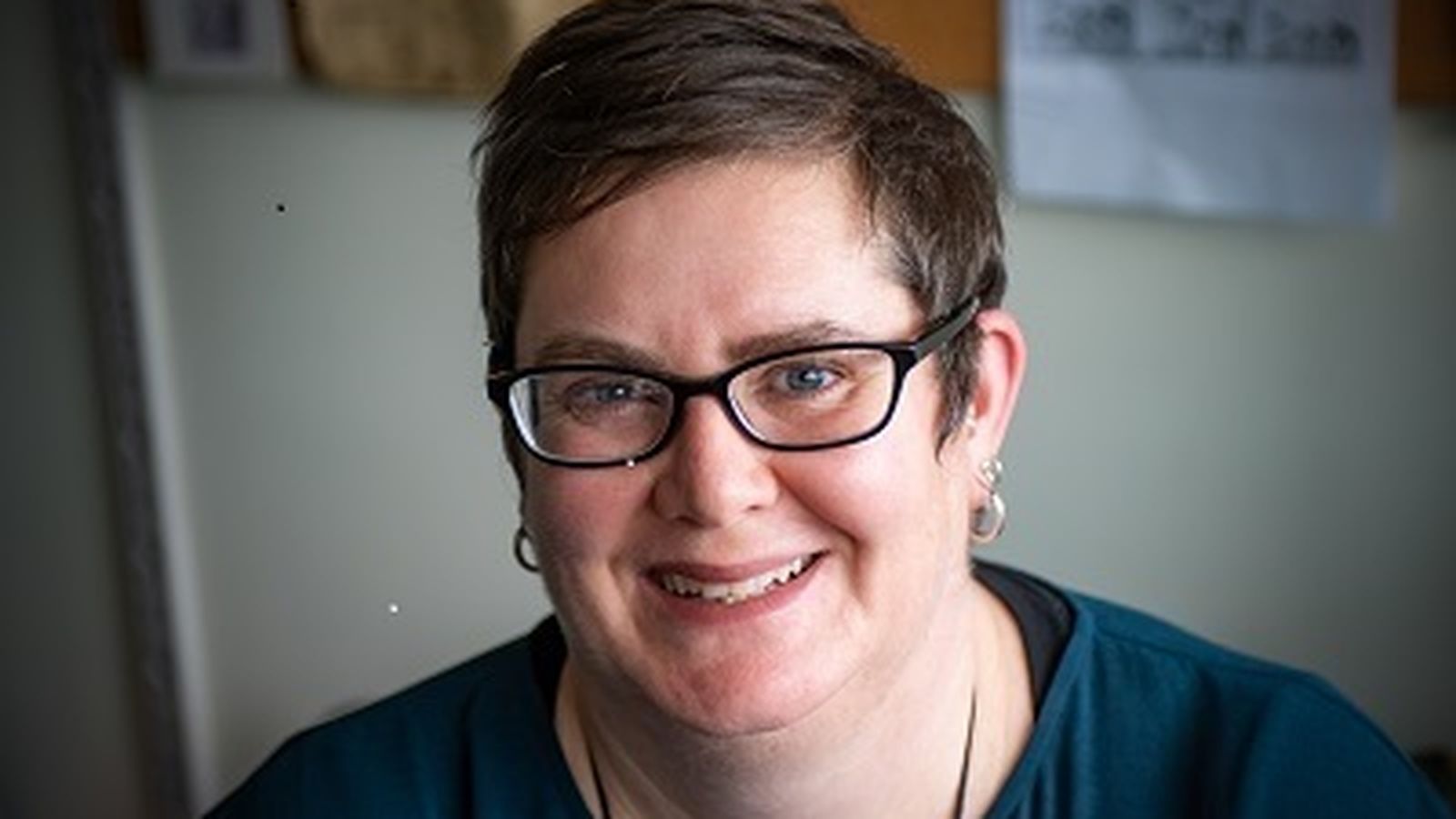 A woman with short brown hair wearing glasses smiles at the camera