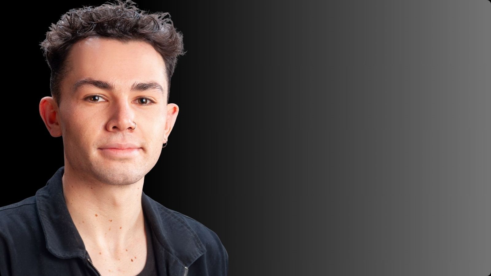 A young man with curly black hair smiles at the camera