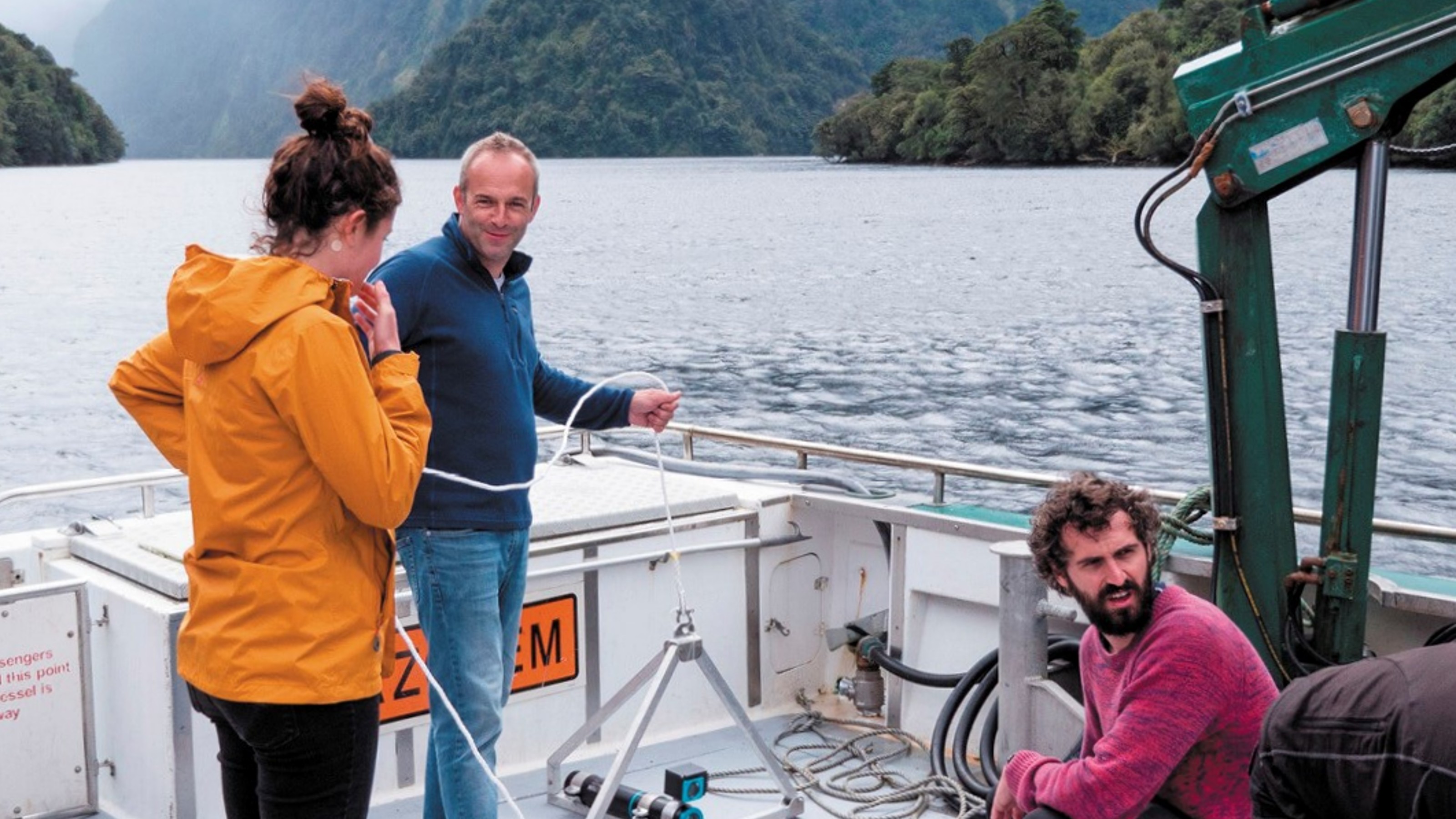 Three people on boat with steep mountains in background
