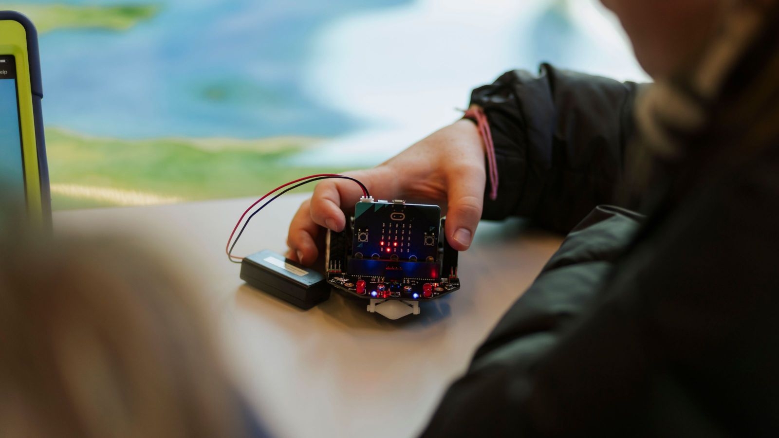 Someone's hand playing with a small robot on a table