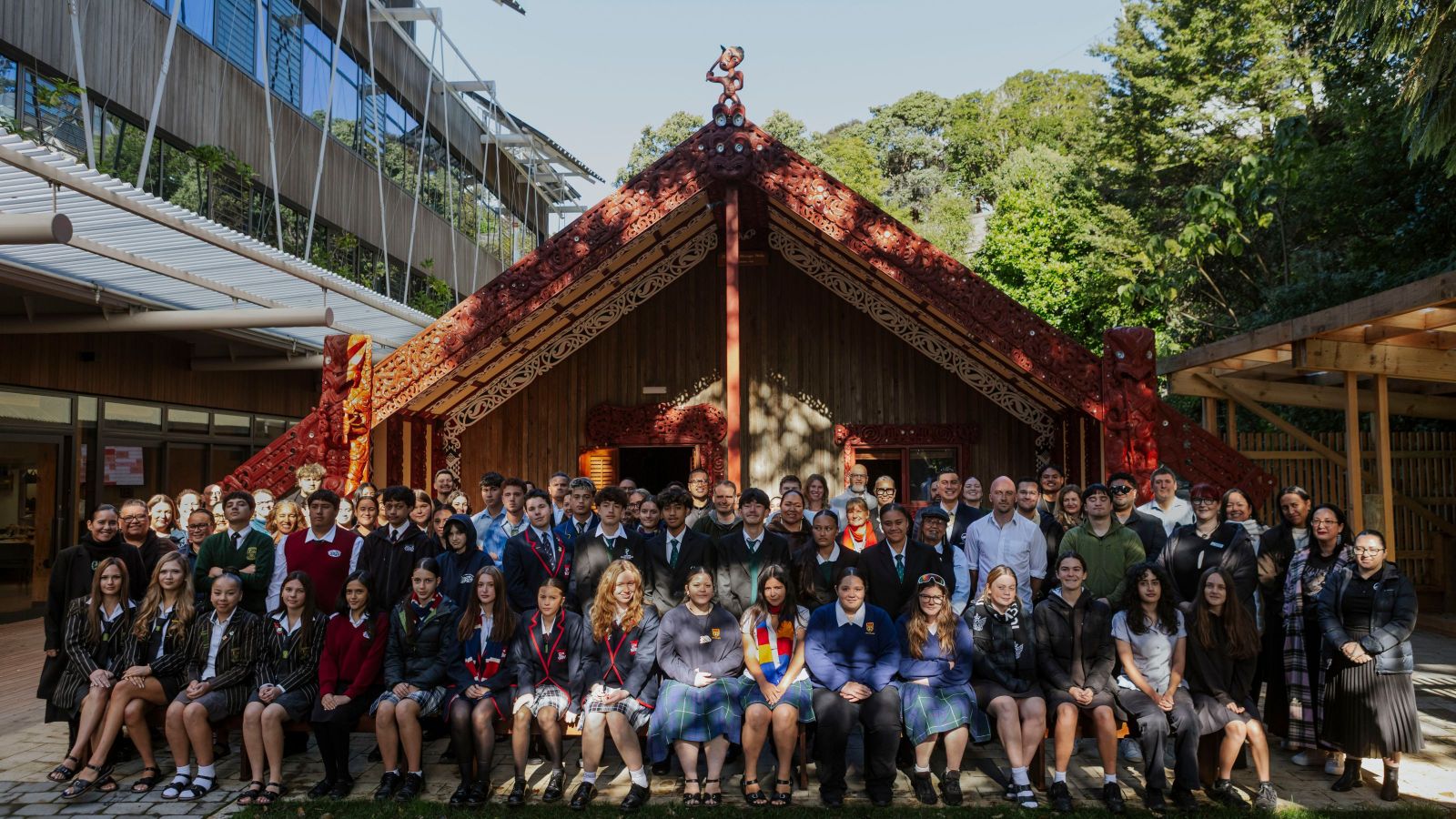Large group of people in front of a wharenui with carvings