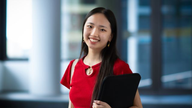 Katie Chu-Fong, dressed in red and holding a folder.