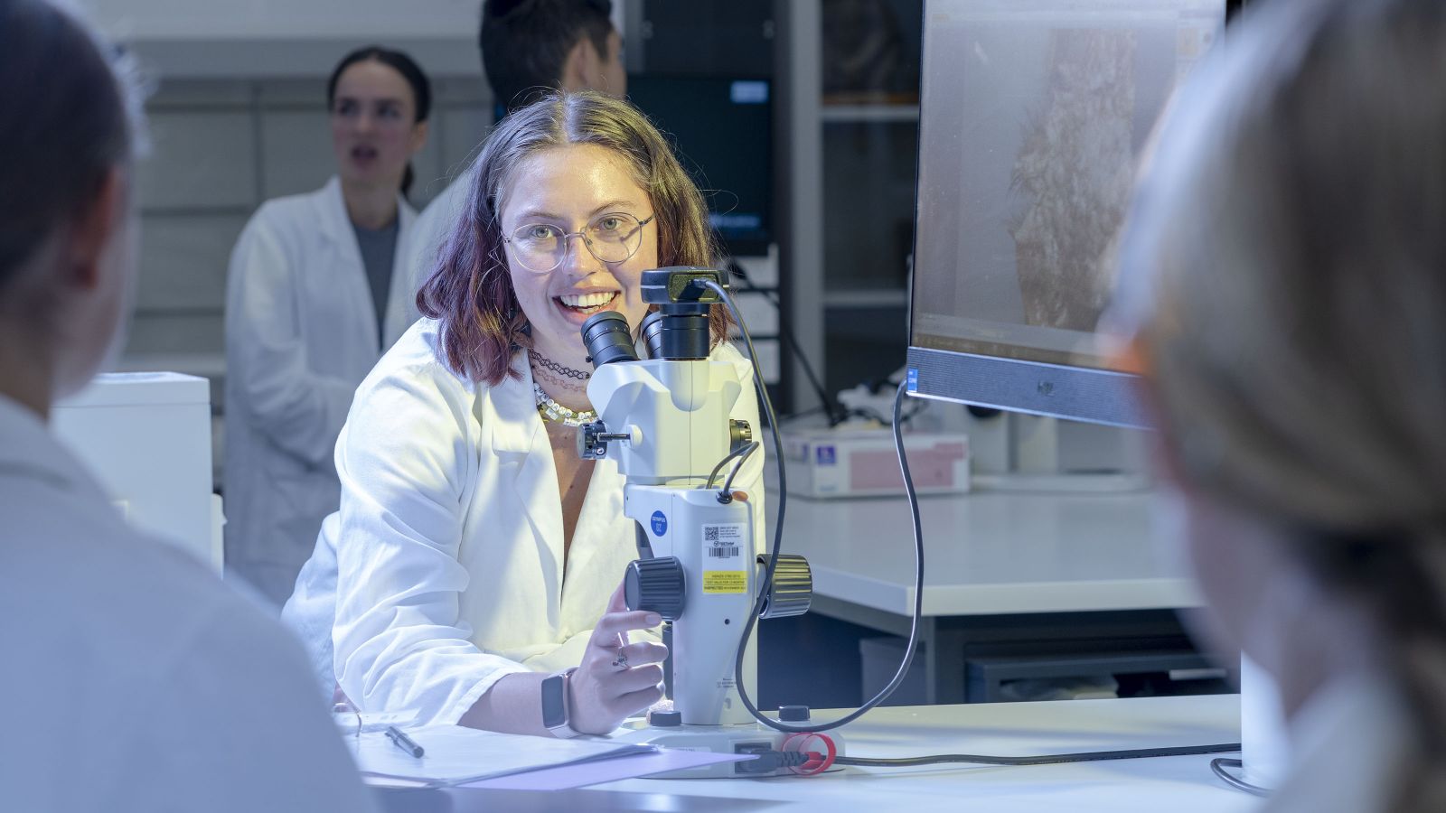 A female student stands behind a microscope
