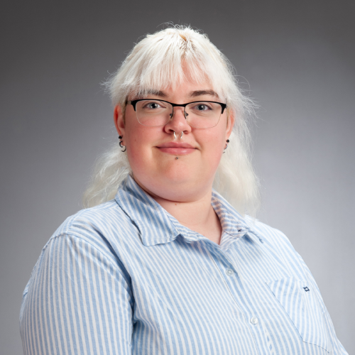 Chemistry PhD student Emma Burdick pictured wearing a blue and white striped button up shirt in front of a grey studio background.