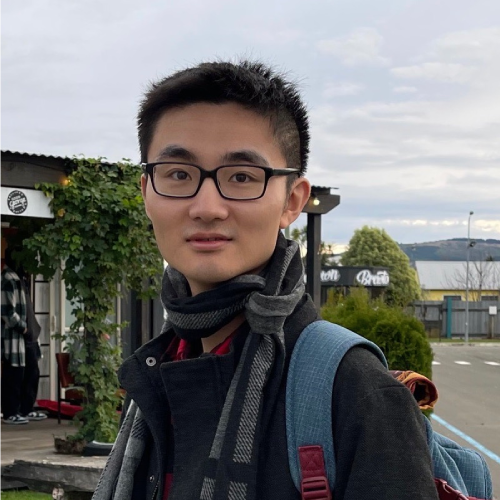 PhD student Kang Wang posing towards camera, wearing a coat, scarf and backpack outside under a blue sky.