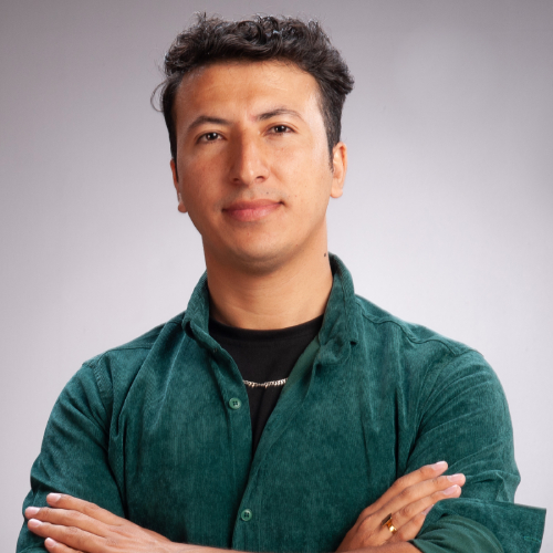 Physics PhD student Sangar Begzaad, wearing a dark green button up shirt and posing with his arms crossed in front of a grey studio background.