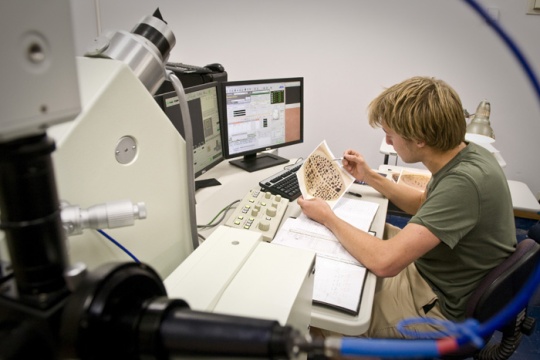 A student examines a piece of paper by computer and lab equipment.