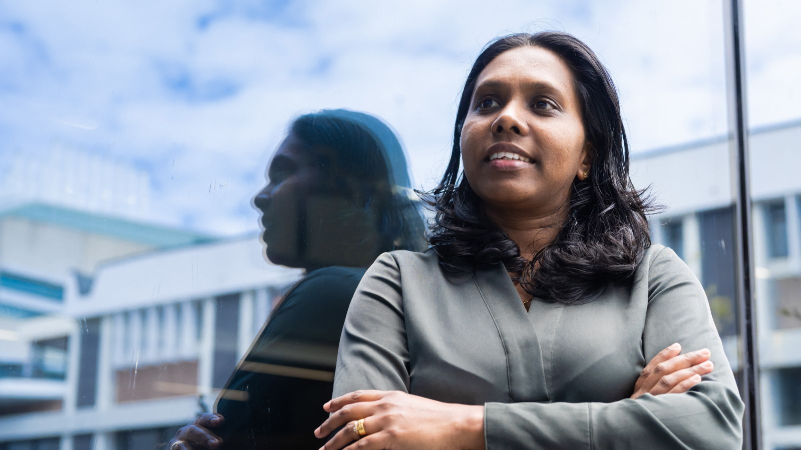 Erandi Nanayakkara, with her arms folded, standing in front of her relection in glass.