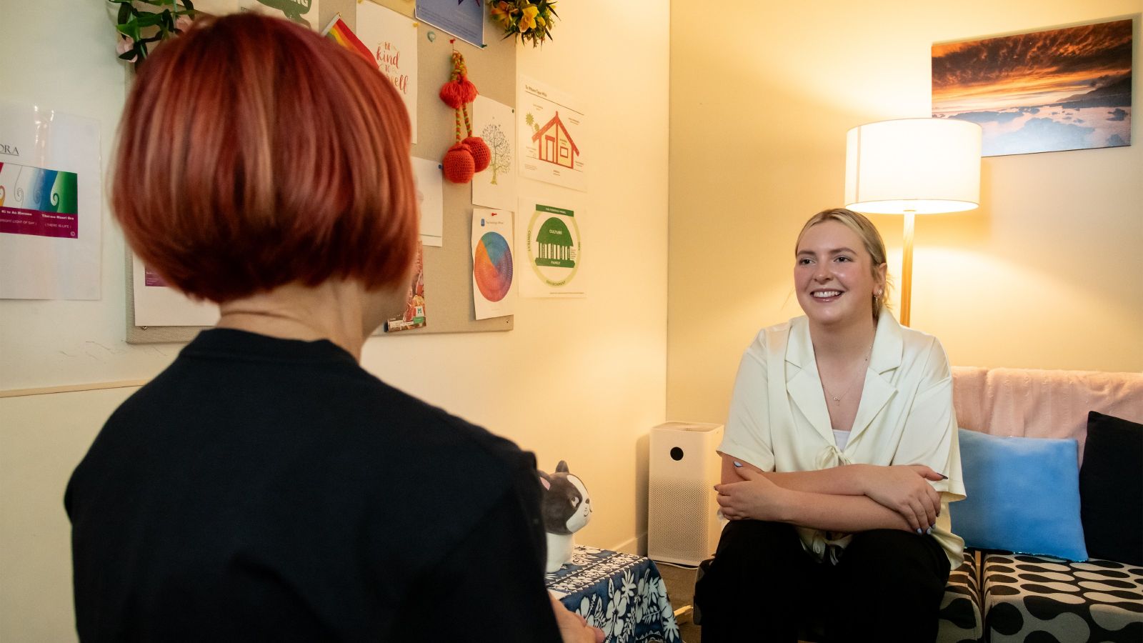 Young woman sitting on a couch smiling and speaking to a lady who is sitting opposite her.