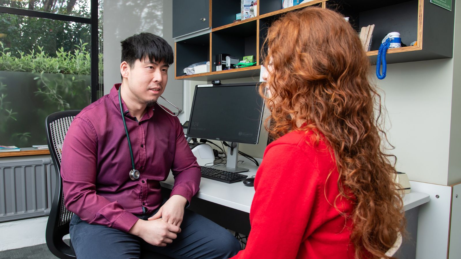 Male doctor sitting on a chair at a desk speaking to a female student.