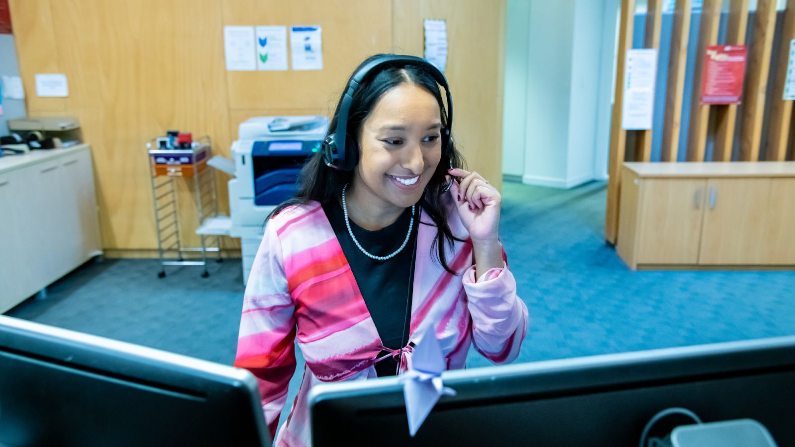 Young female sitting at desk smiling with headset on.