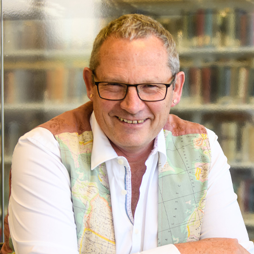James Renwick smiles to the camera. He is wearing a waste coat designed from a world map material