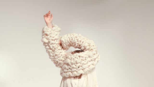 A person pulls a jumper made out of felted wool waste over their head. The garment is part of Charlie Walkley's design project 'Felt the Earth'.