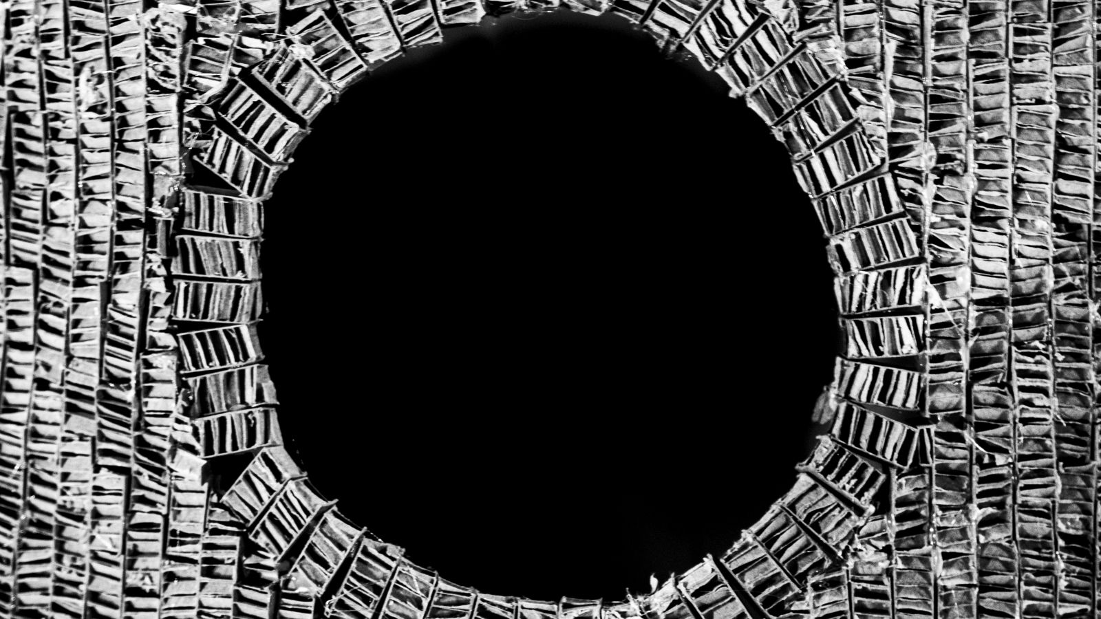 Black an white close up imageof a cardboard model with layered texture and a circle cut out in the middle