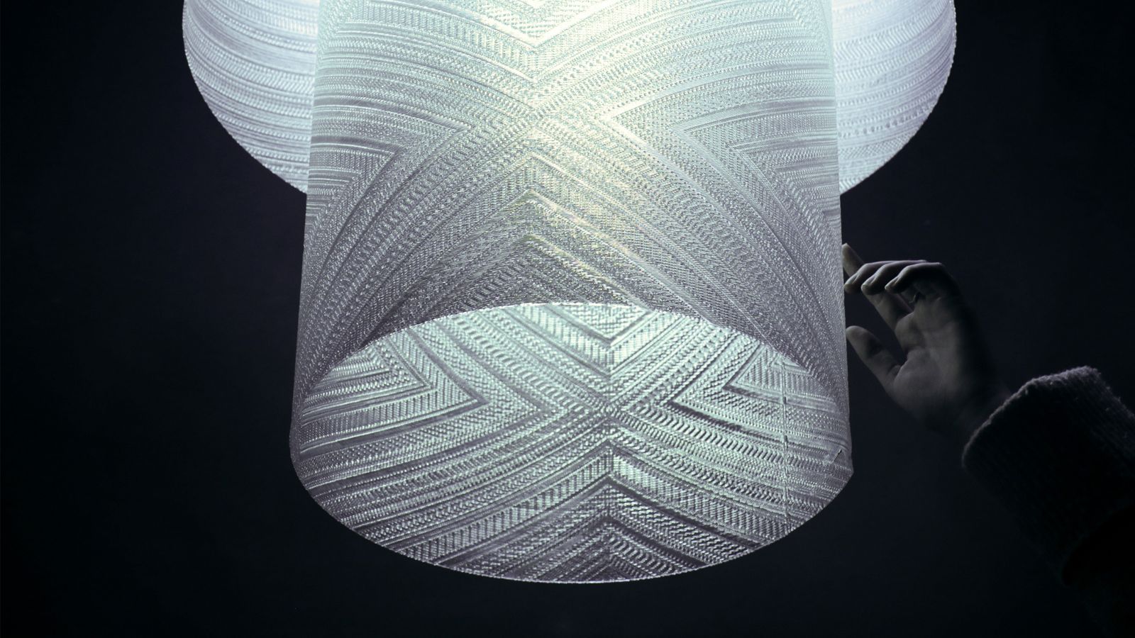 Image of a 3D printed textured light shade with a hand reaching for it.