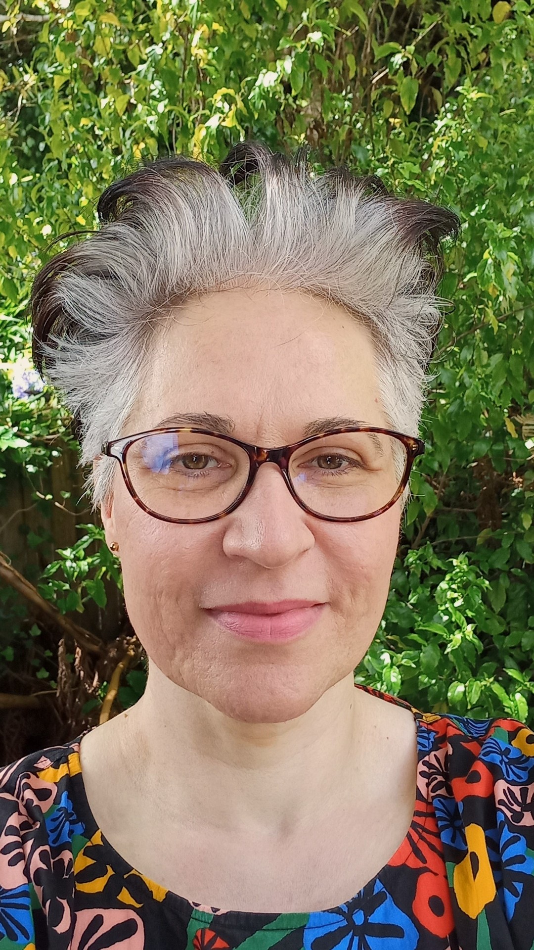 A profile photo of Emina Petrovic, wearing a colourful top, with foliage in the background.